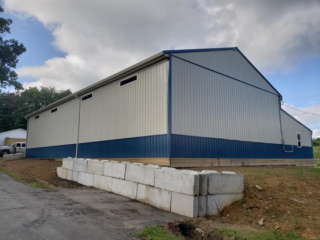 A metal barn with white upper walls and blue lower panels stands behind a short retaining wall made of concrete blocks.