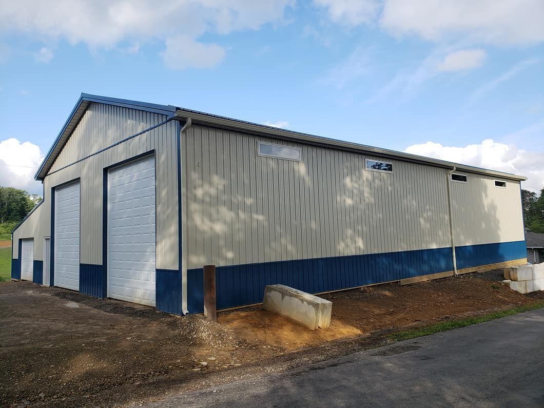 A tan metal warehouse with blue trim and two large roll-up doors, set against a blue, partly cloudy sky.
