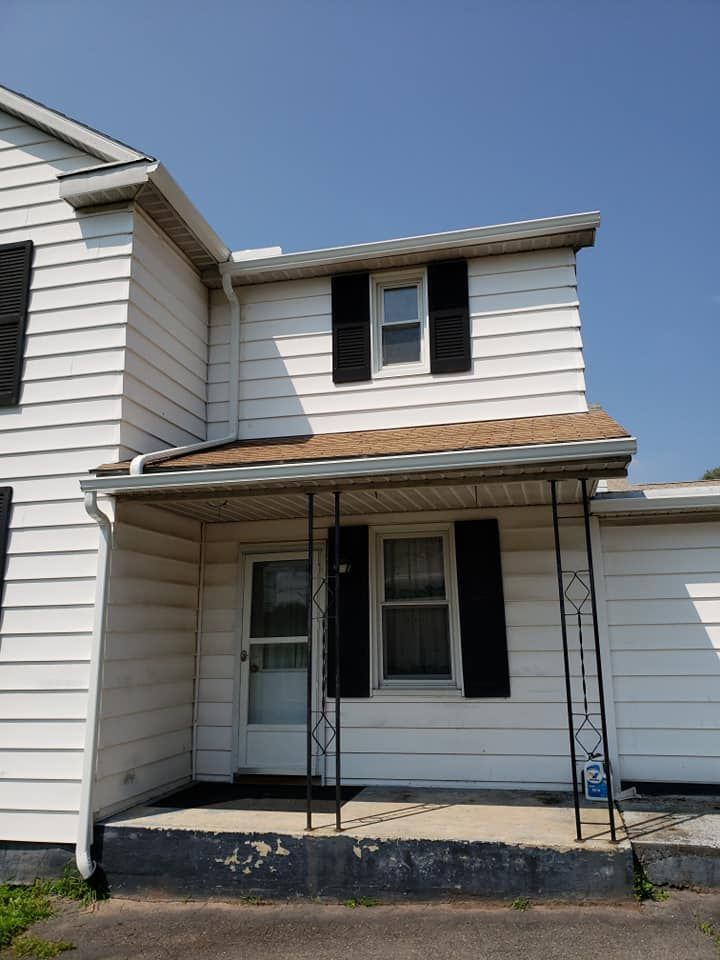 A white house with black shutters, a small front porch, iron pillars, and a concrete stoop against a clear blue sky.