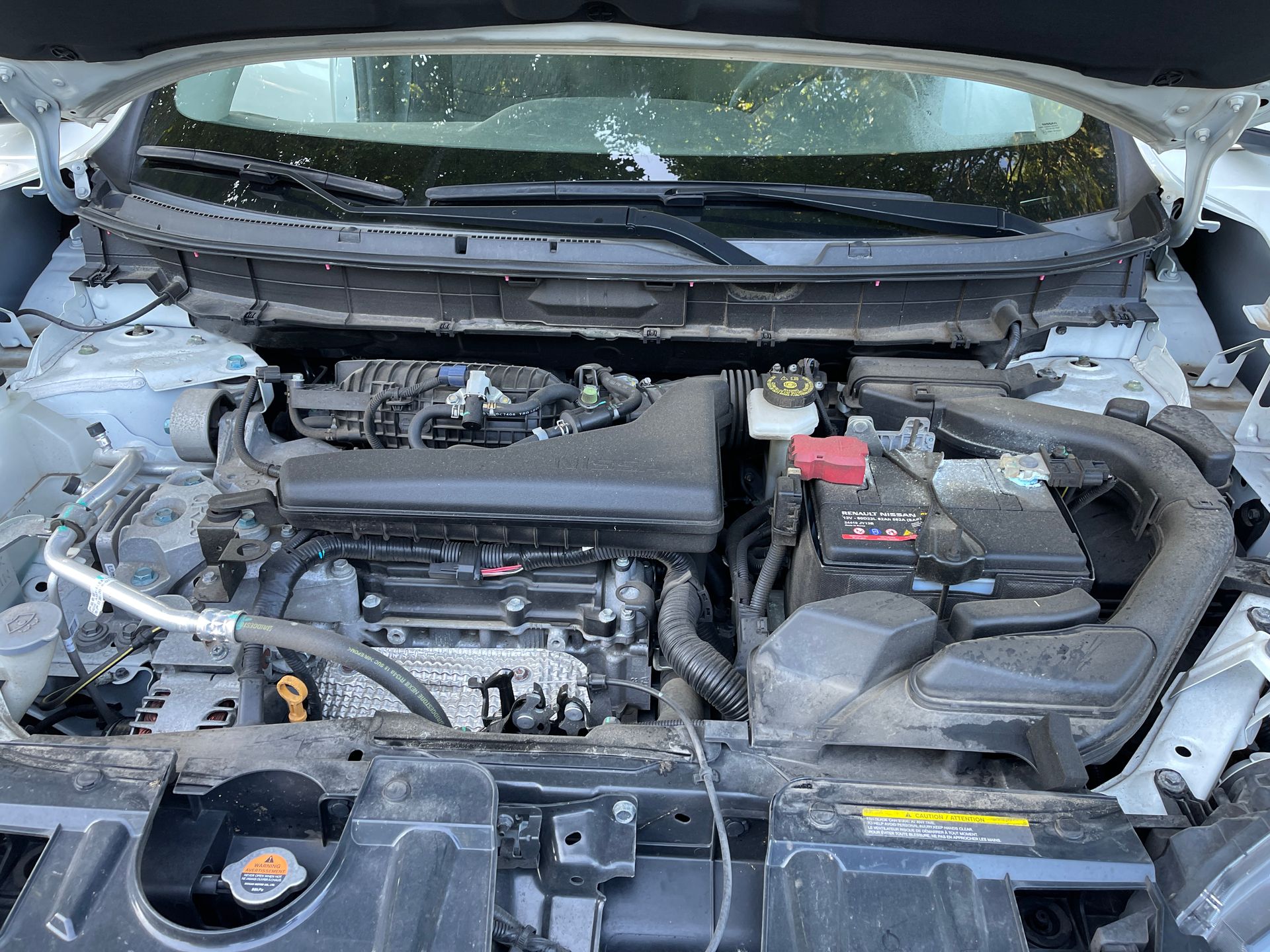 The engine of a nissan rogue is shown with the hood open.