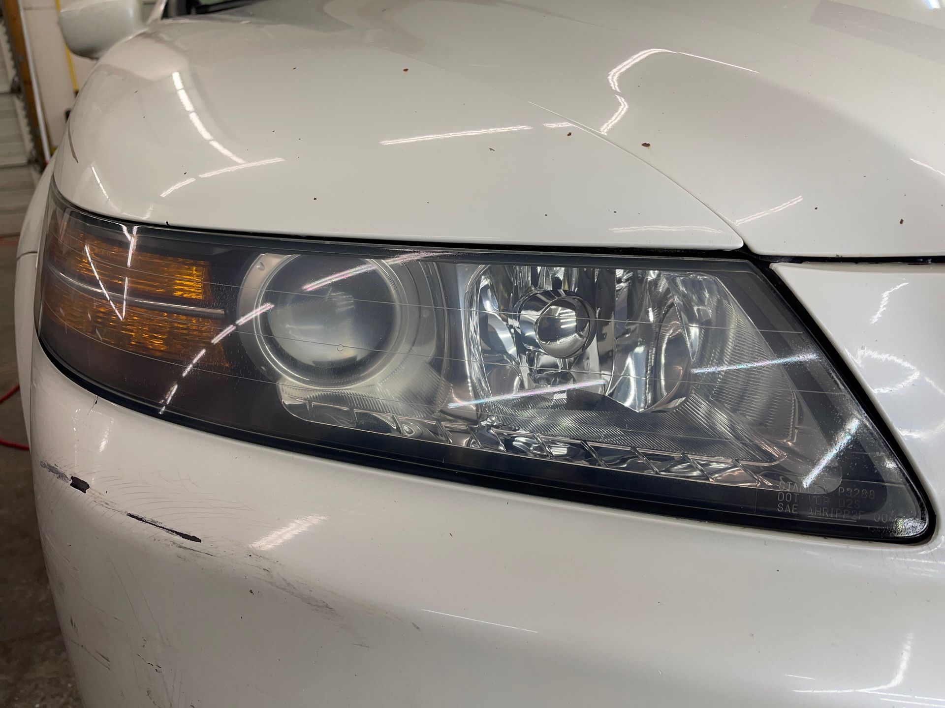 A close up of a white car 's headlight in a garage.