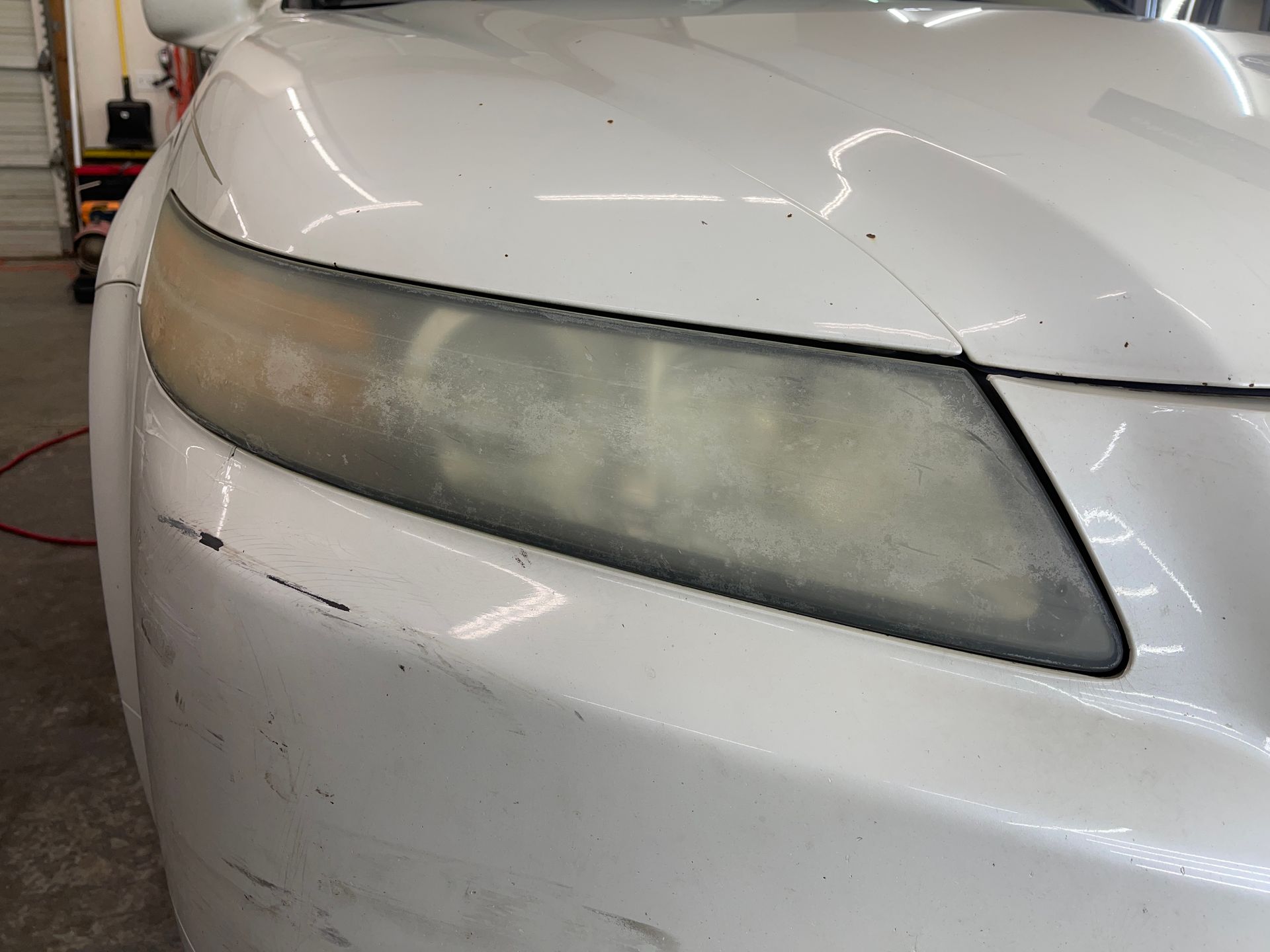 A white car with a dirty headlight is sitting in a garage.