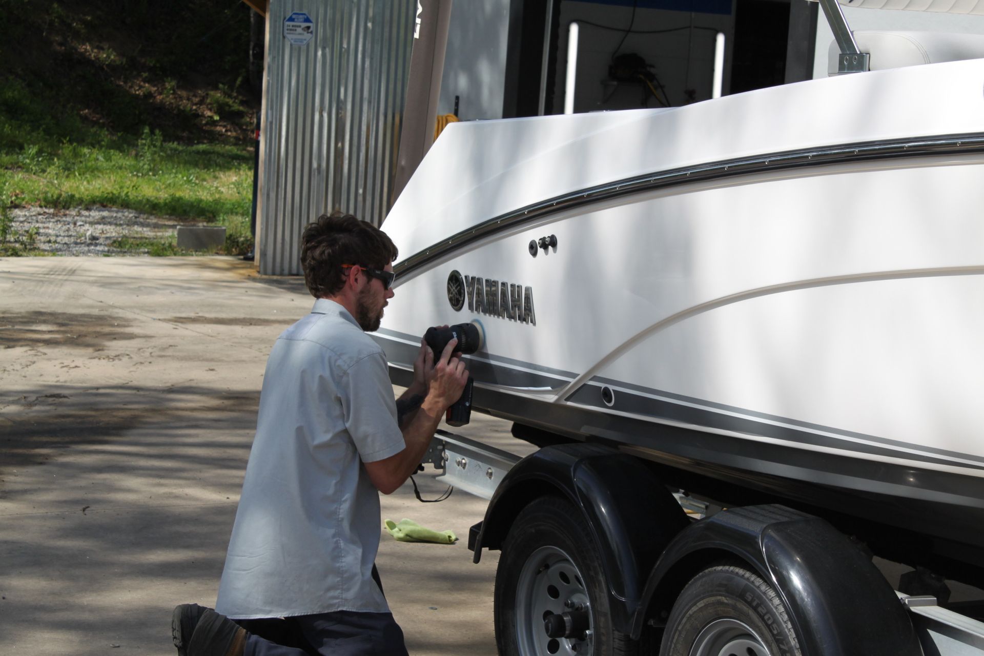 Person kneeling beside a white Yamaha boat on a trailer, examining the hull outdoors