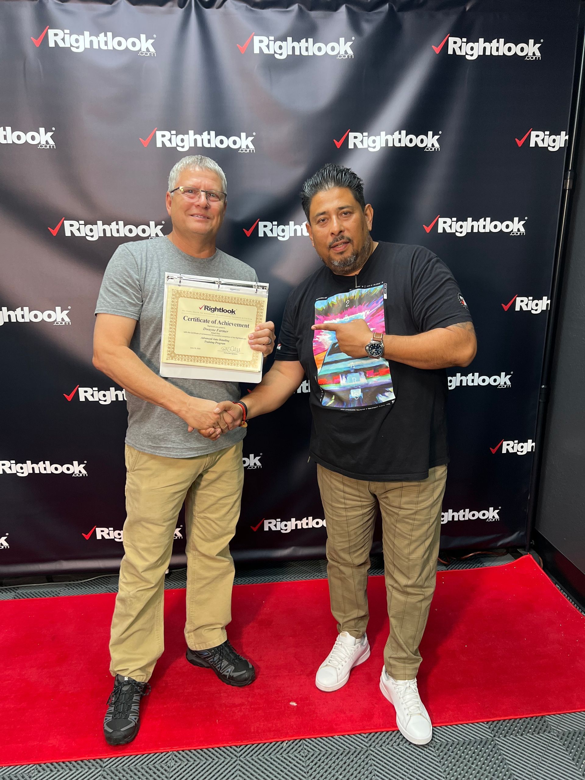 Two men are standing next to each other on a red carpet holding a certificate.