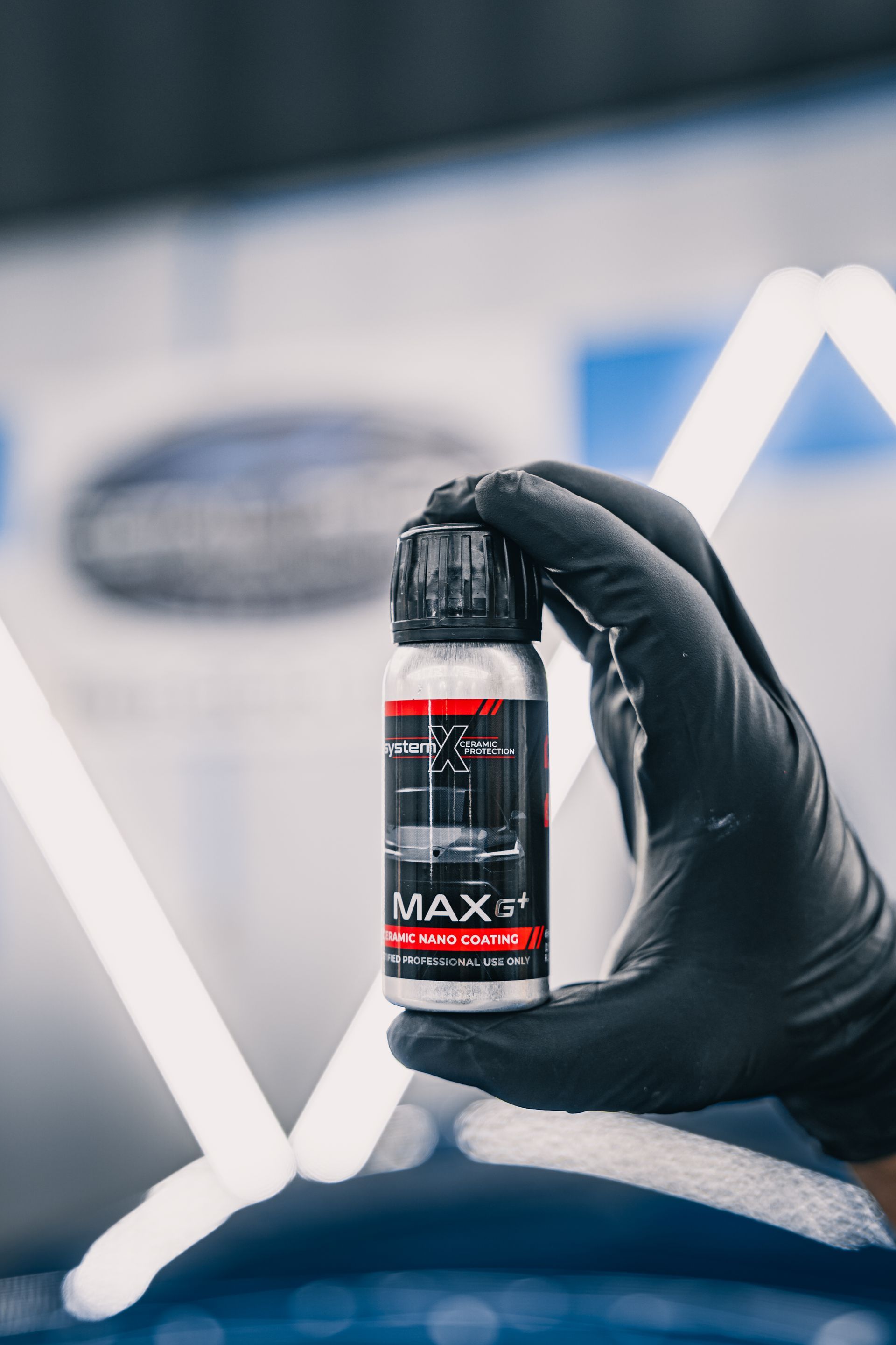 Gloved hand holding a bottle of MAX car detailing product against a blurred background.