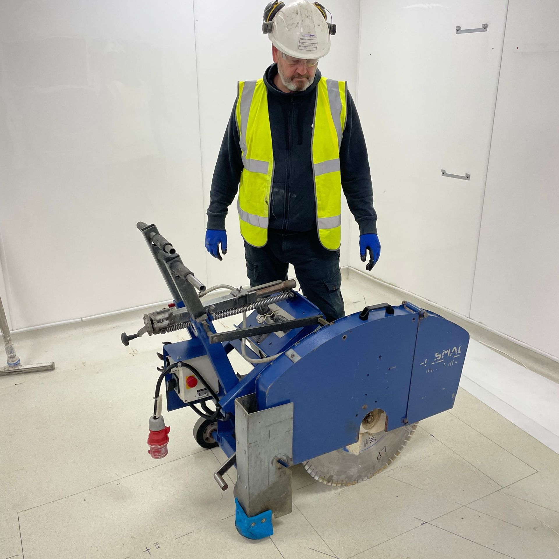 A man wearing a hard hat and safety vest is standing next to a machine.