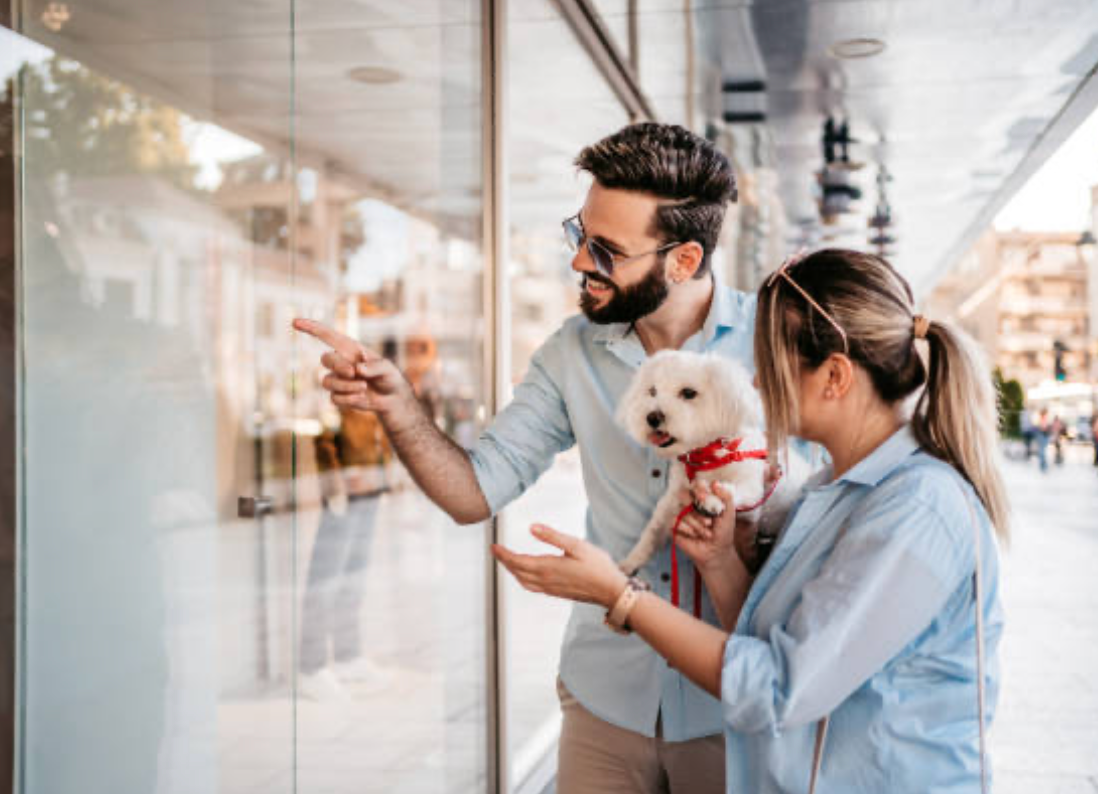 a photo of a couple holding a dog and looking at the mall window