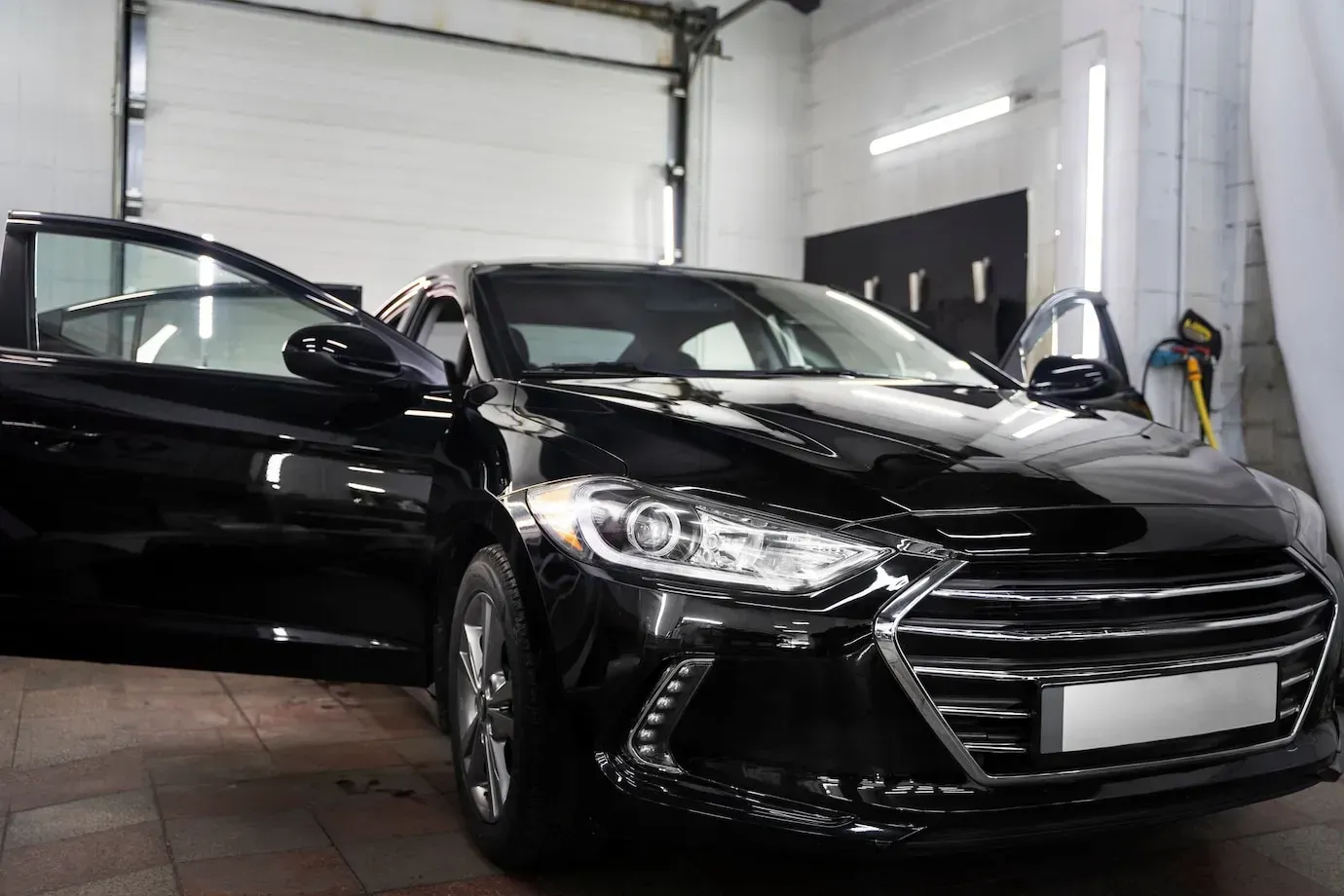 A black car is parked in a garage with its doors open.