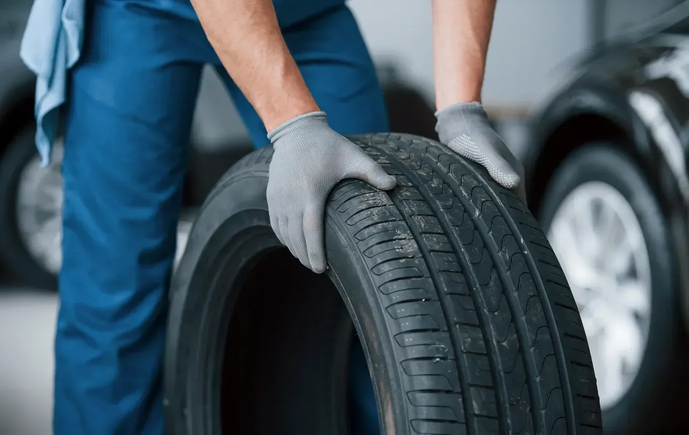 A man wearing gloves is holding a tire in his hands.