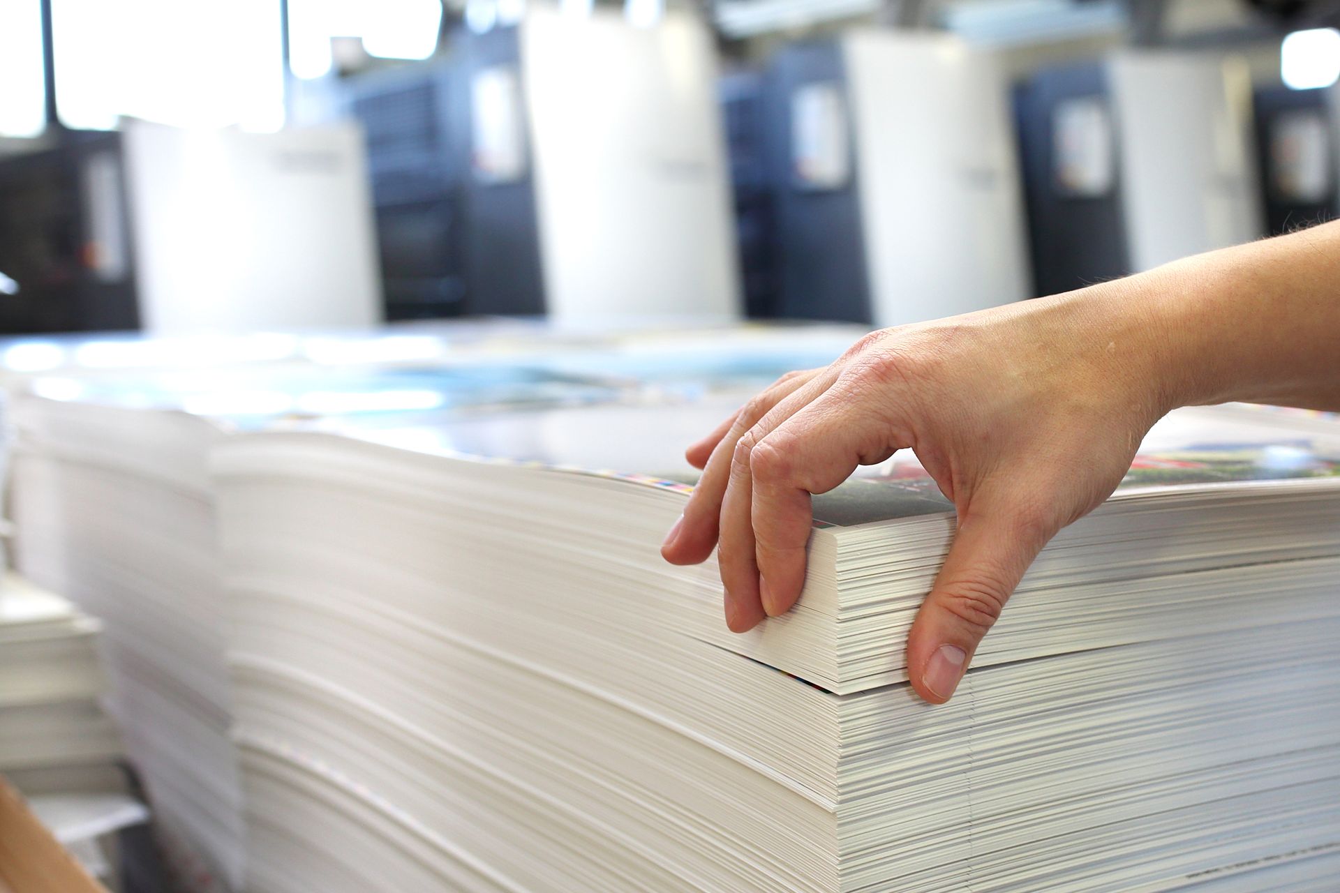 Hand placing sheets of paper on a stack in a printing or paper production facility