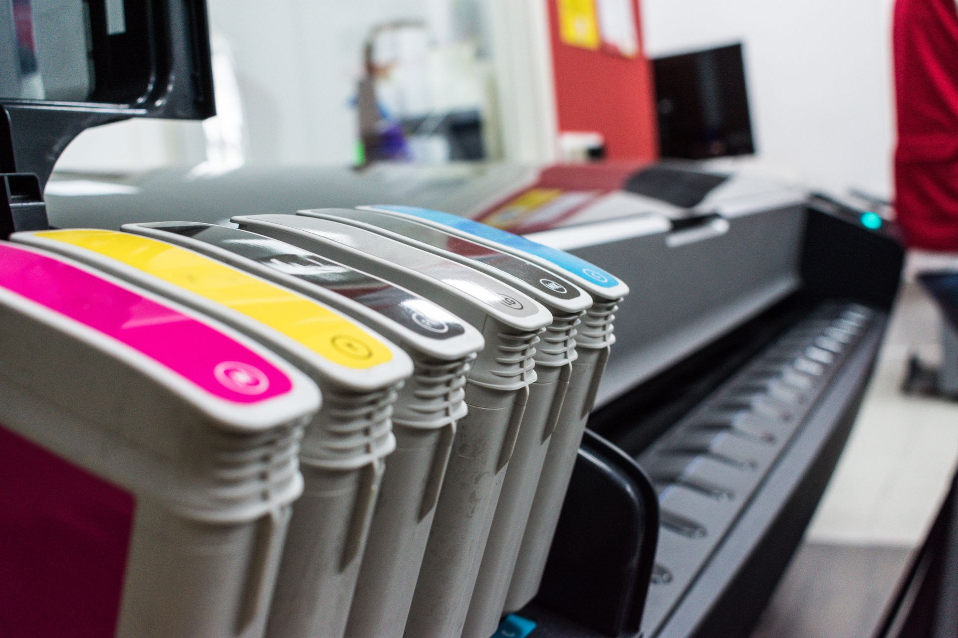 Color-coded printer ink cartridges lined up beside a wide-format printer in a print shop.