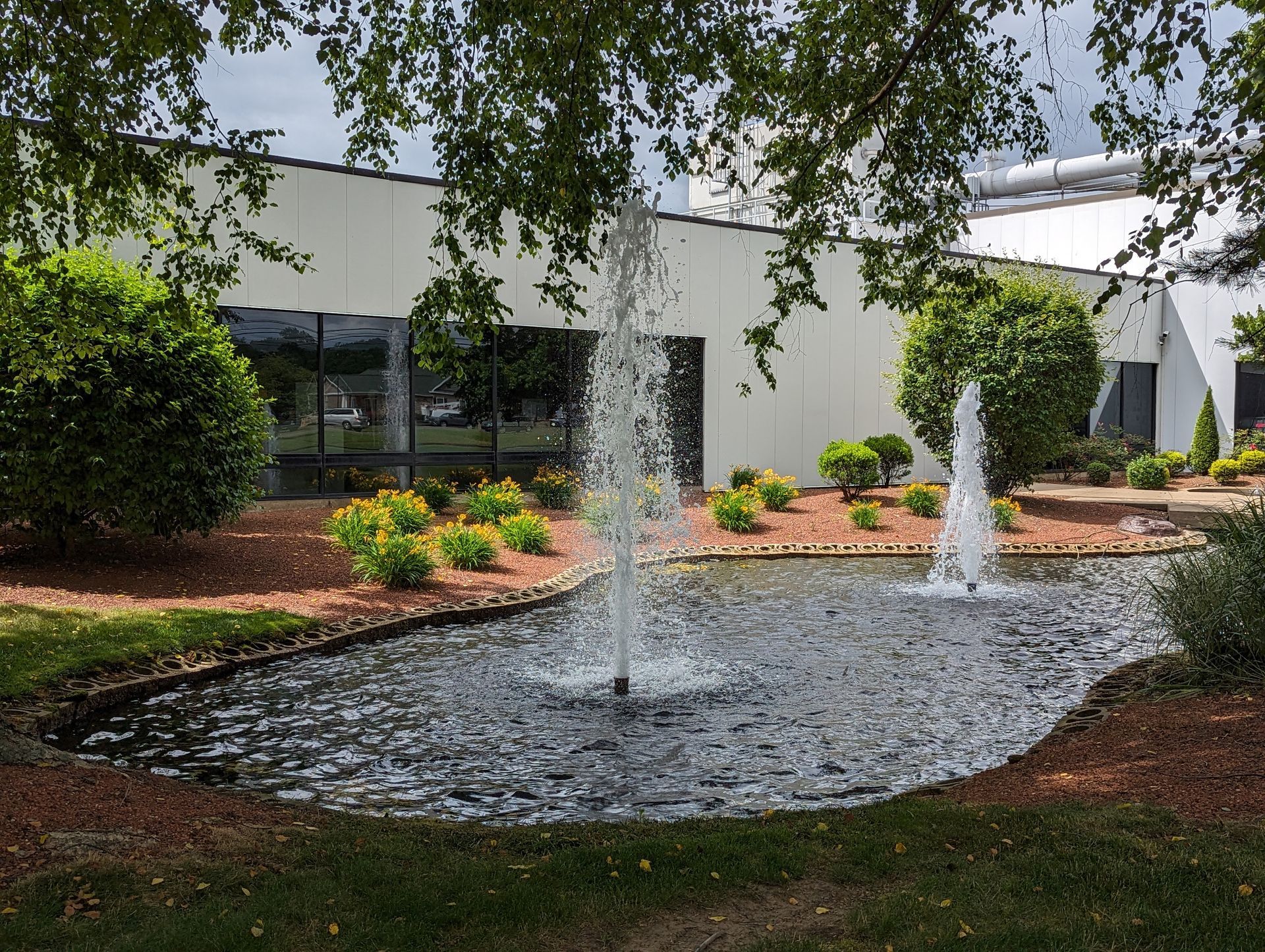 There is a fountain in the middle of a pond in front of a building.
