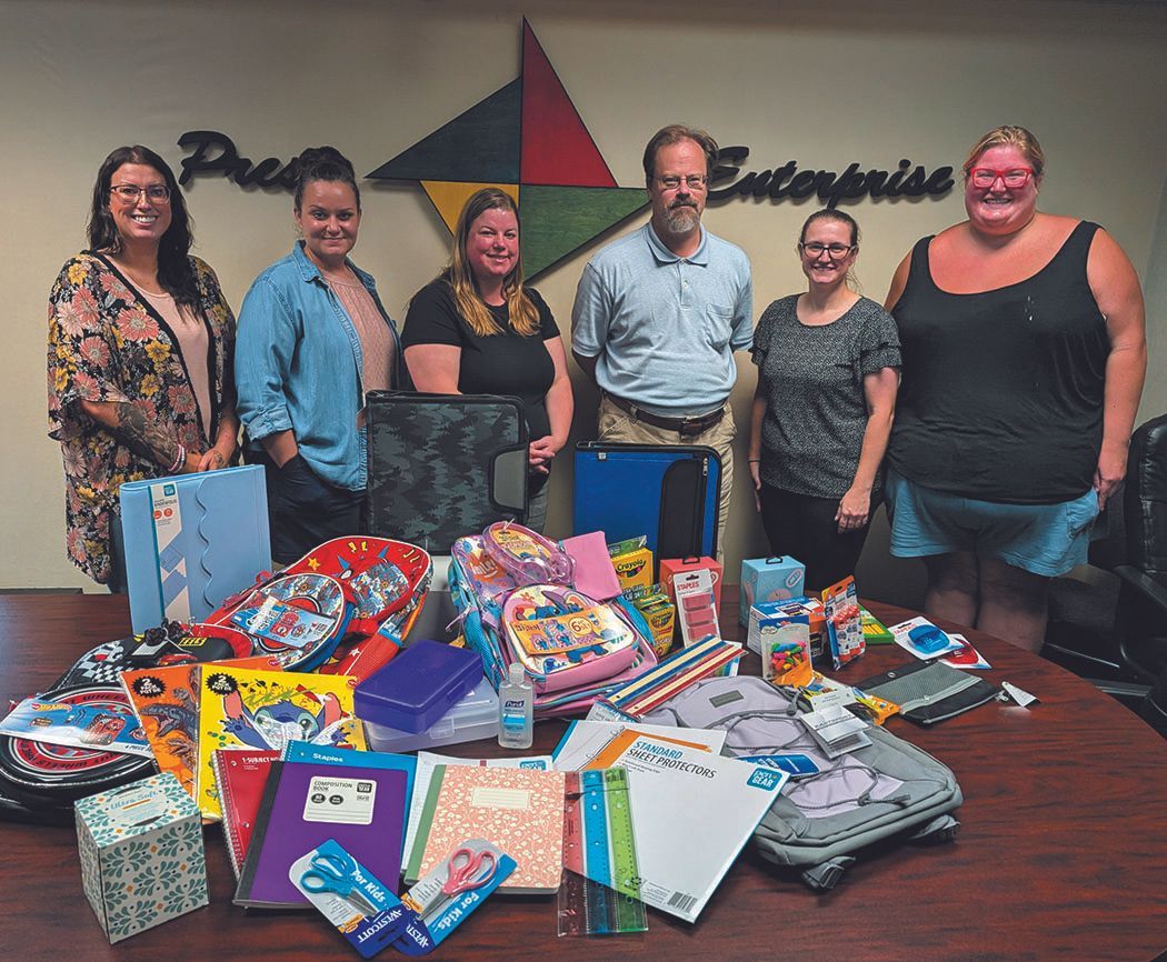 People standing behind a table piled with school supplies. A logo reading