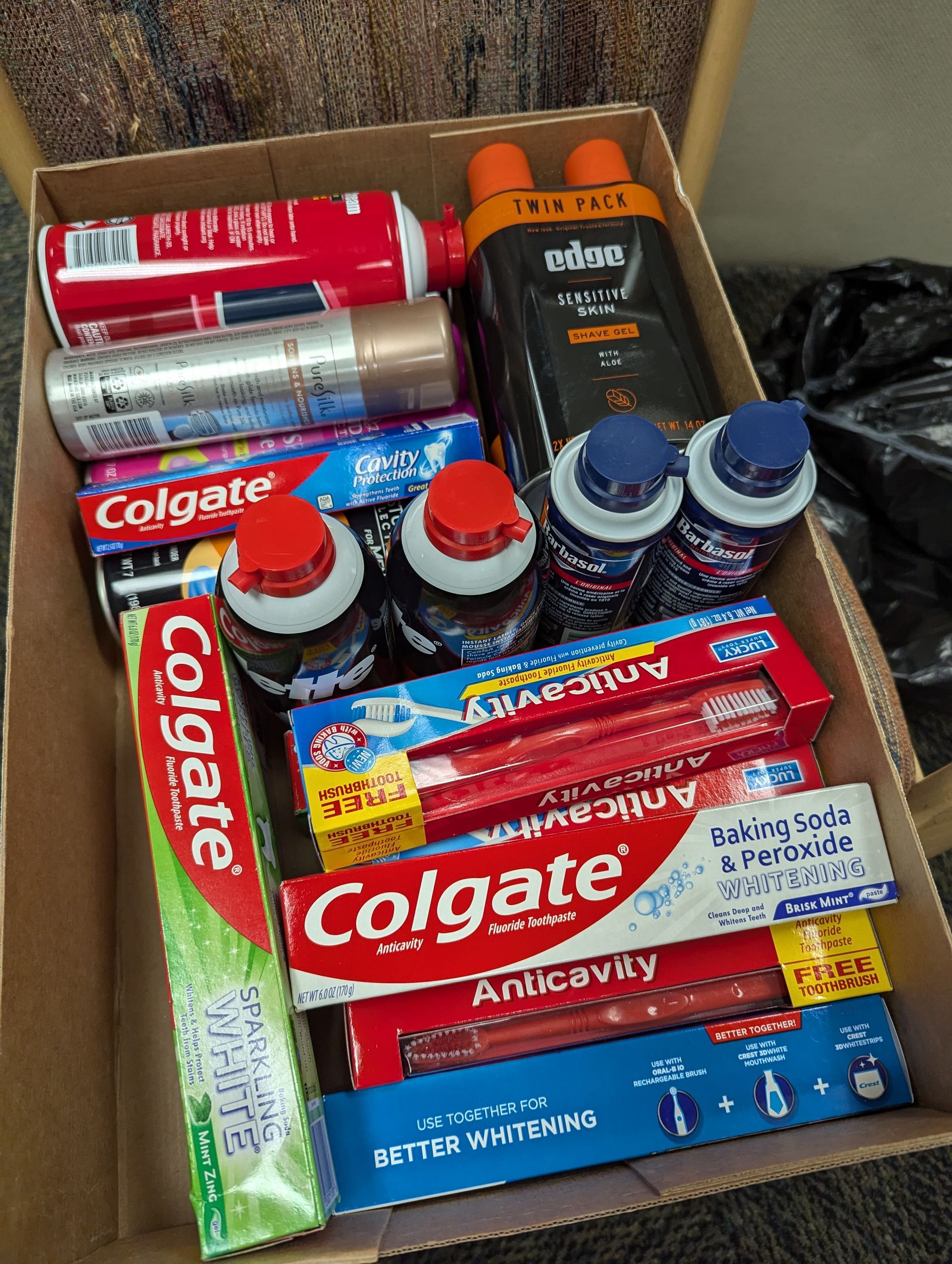 Box filled with toiletries: shaving cream, toothpaste, and shampoo.