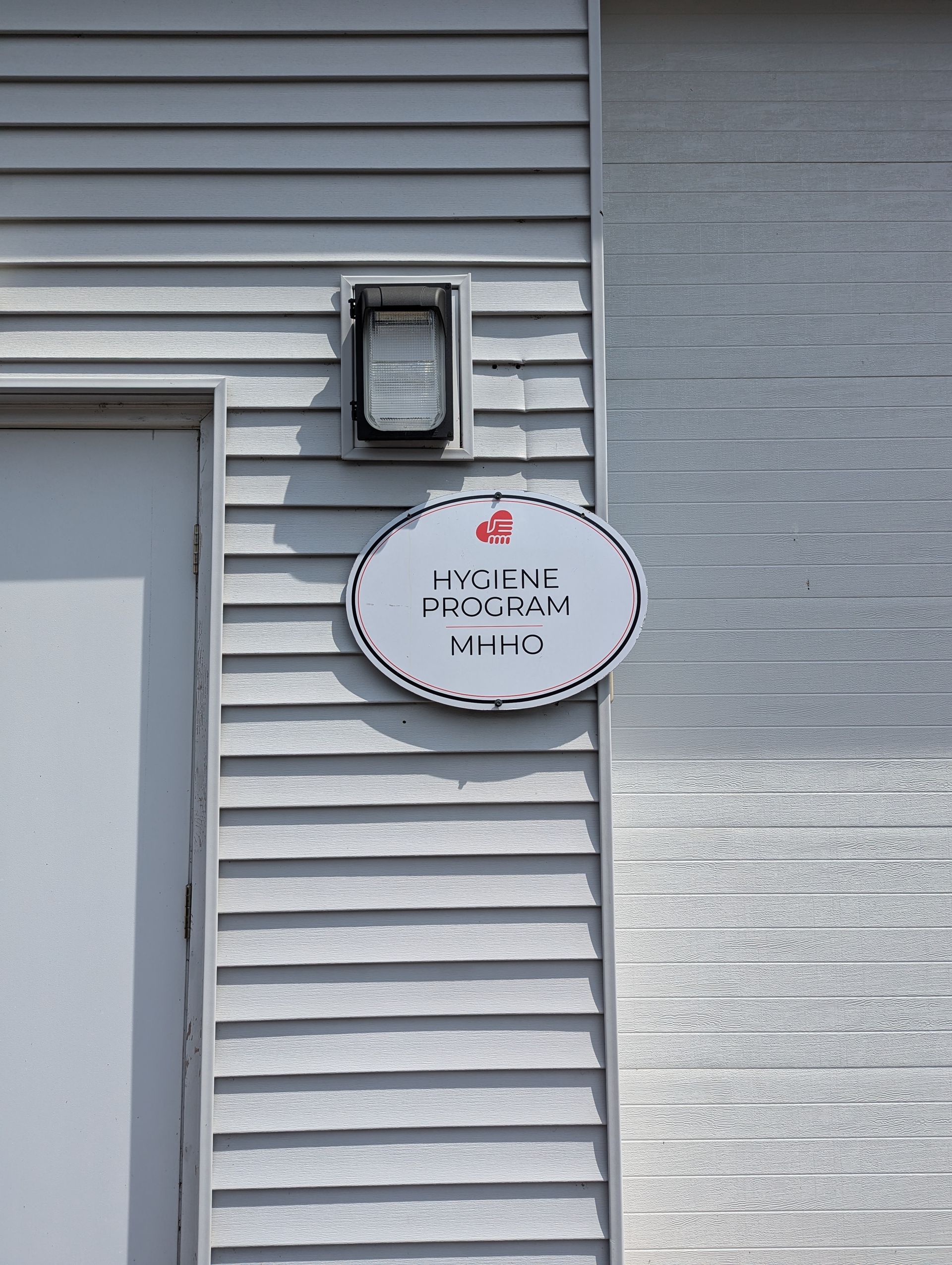 Sign on a gray building with an oval sign, text, and a red cross. Door and light above it.