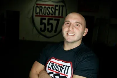 Smiling man in a black CrossFit T-shirt in front of a CrossFit 557 sign