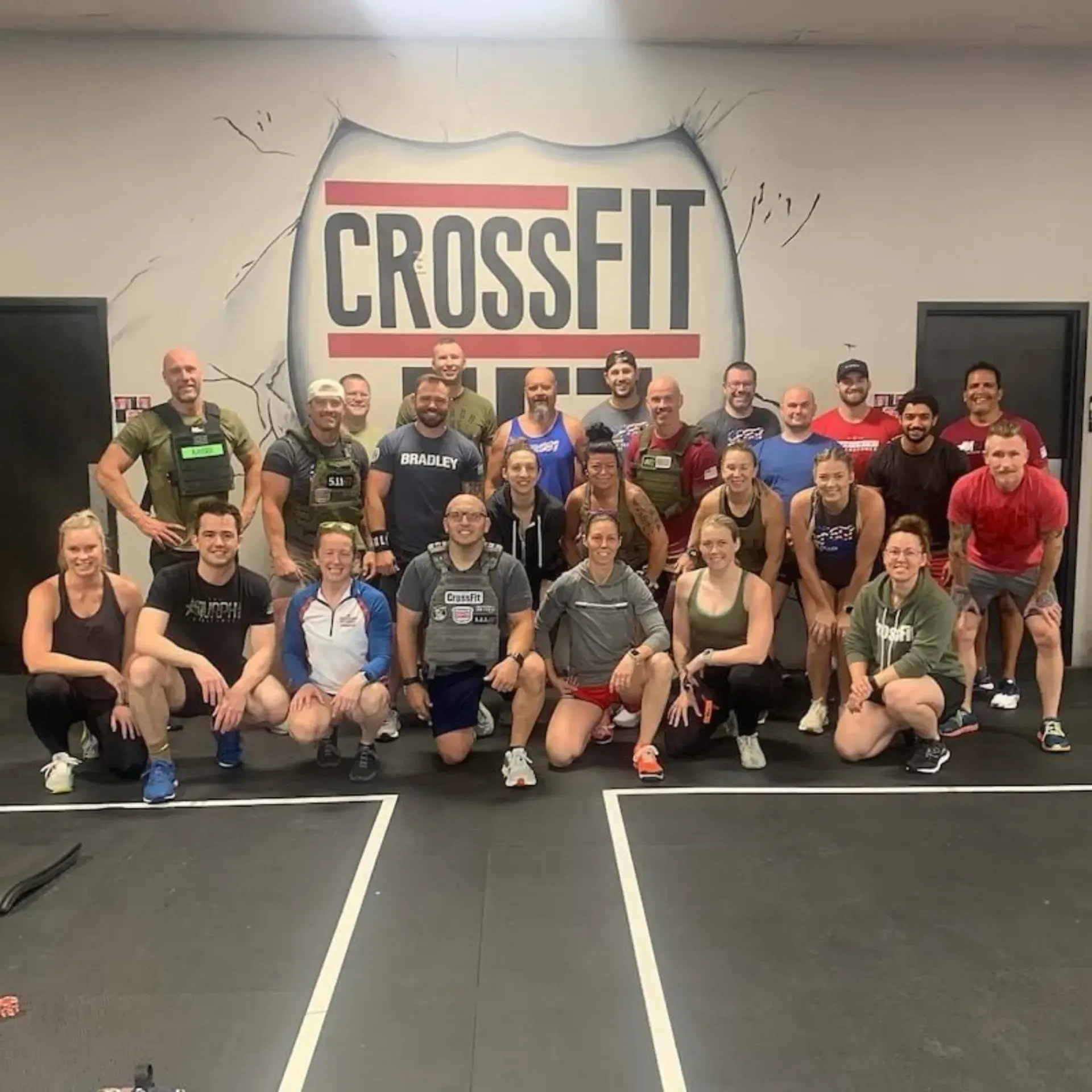 Group of people posing in a CrossFit gym in front of a large “CROSSFIT” wall sign.
