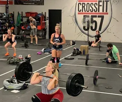 People exercising with barbells in a CrossFit gym, with a large “CrossFit 357” sign on the wall.