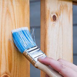 A person is painting a wooden railing with a blue brush.