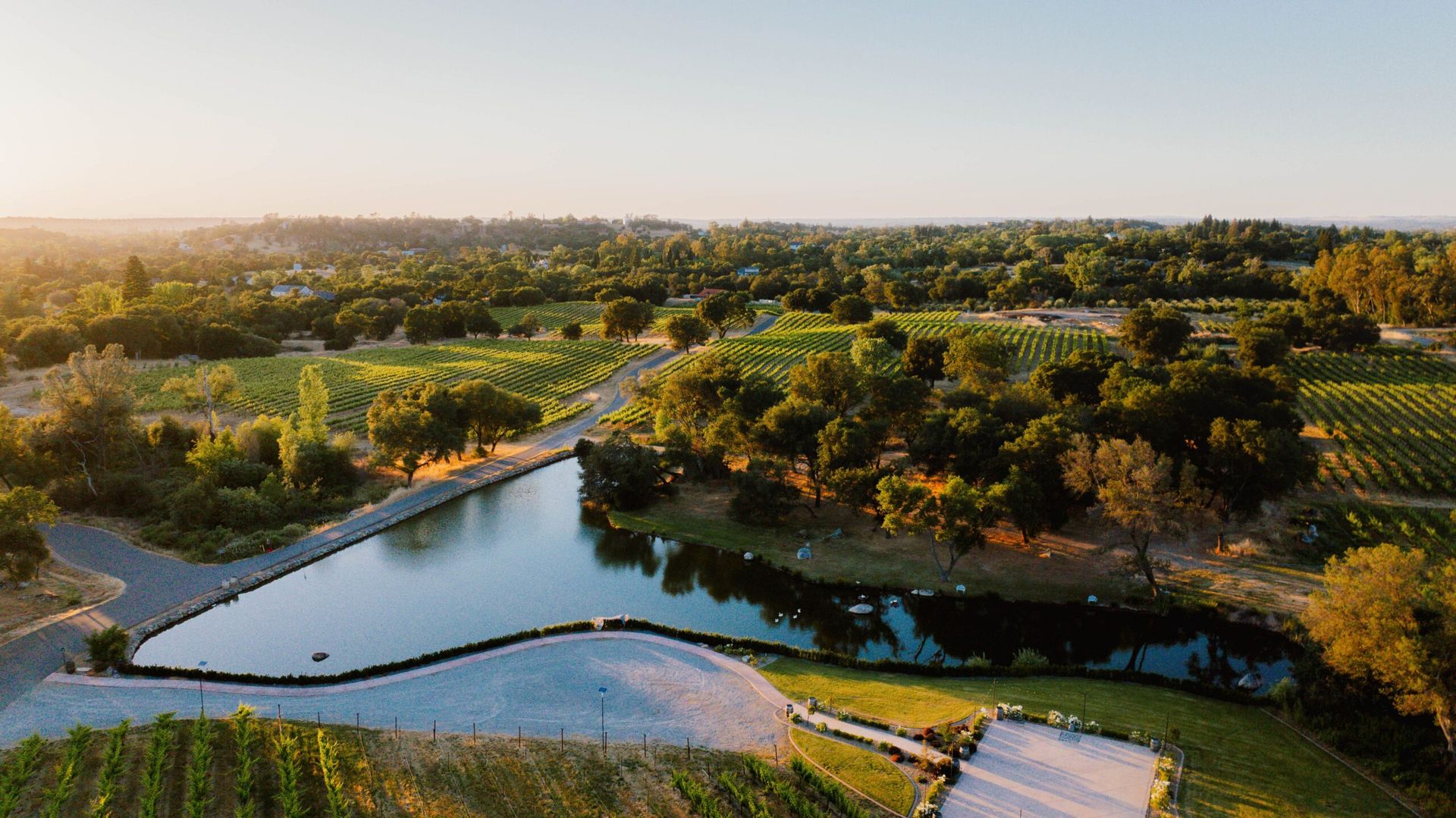 Sunset over a winding river through lush green fields and trees, with a small bridge in the foreground