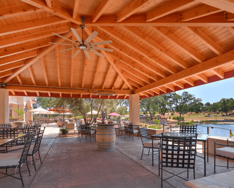 Wooden outdoor pergola with tables and chairs in a shaded patio area
