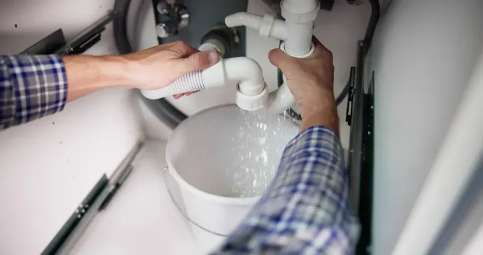 Person fixing a leaking sink drain with a bucket catching water