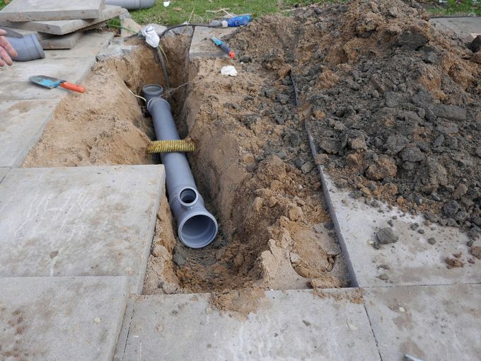 Green hose lowered into open manhole on concrete surface
