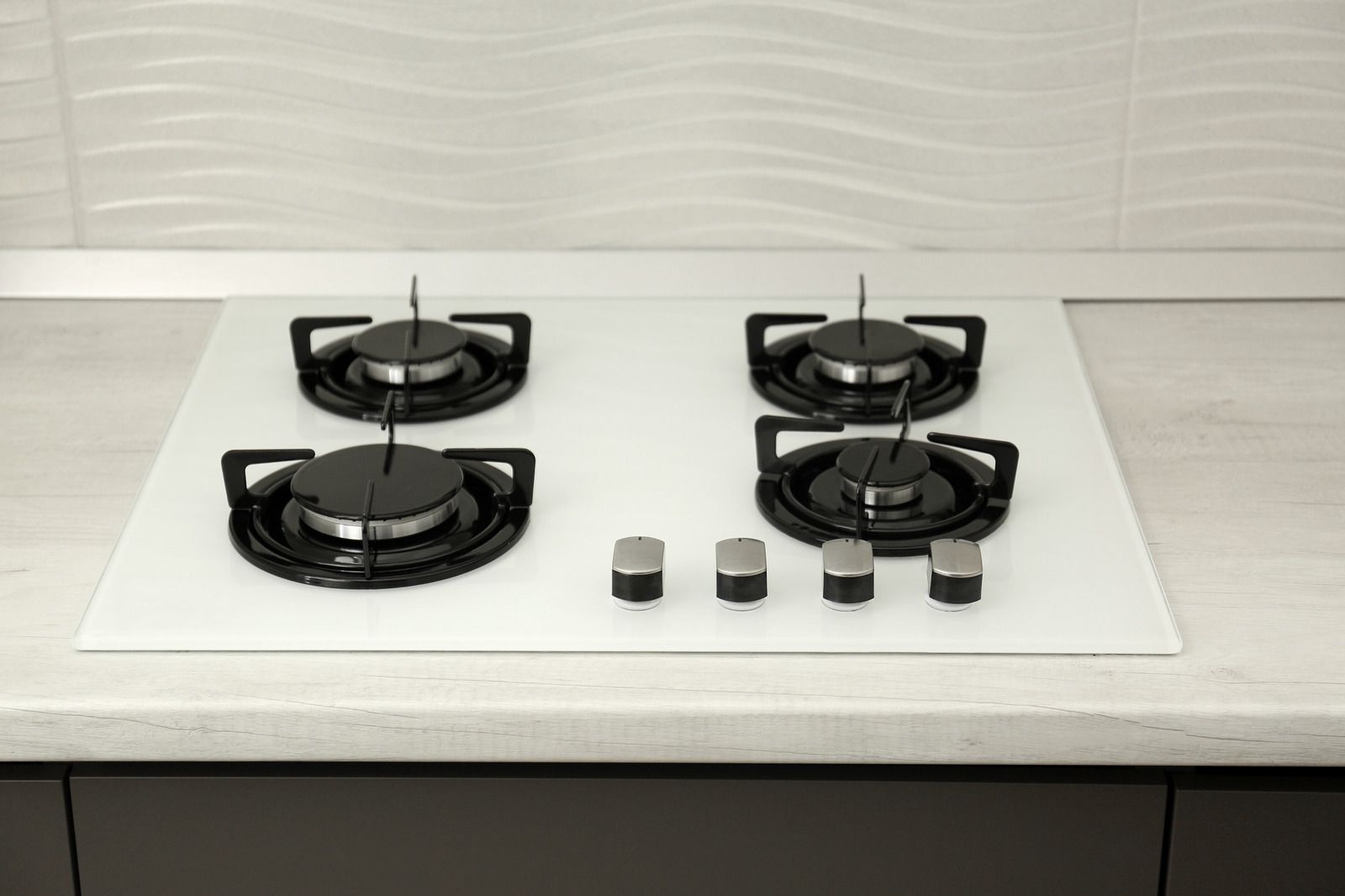Modern white countertop with a four-burner black gas cooktop and silver control knobs