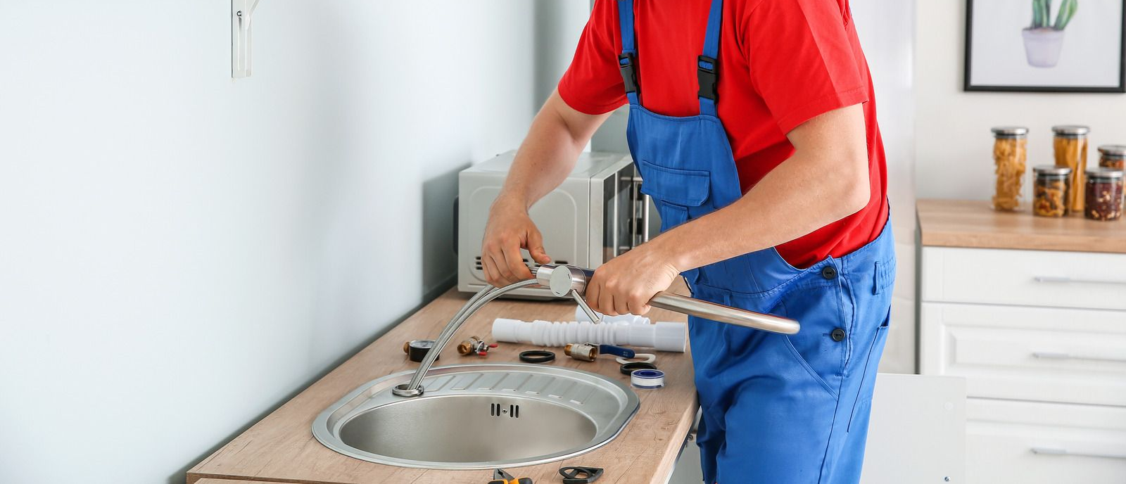 Worker in blue overalls installing a kitchen sink countertop with tools.