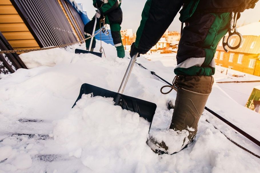 People shoveling snow from a rooftop with a black snow shovel