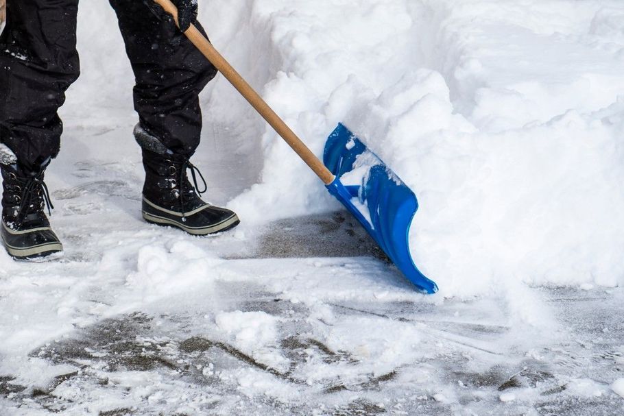 Person shoveling snow with a blue shovel, clearing ice from a snowy ground