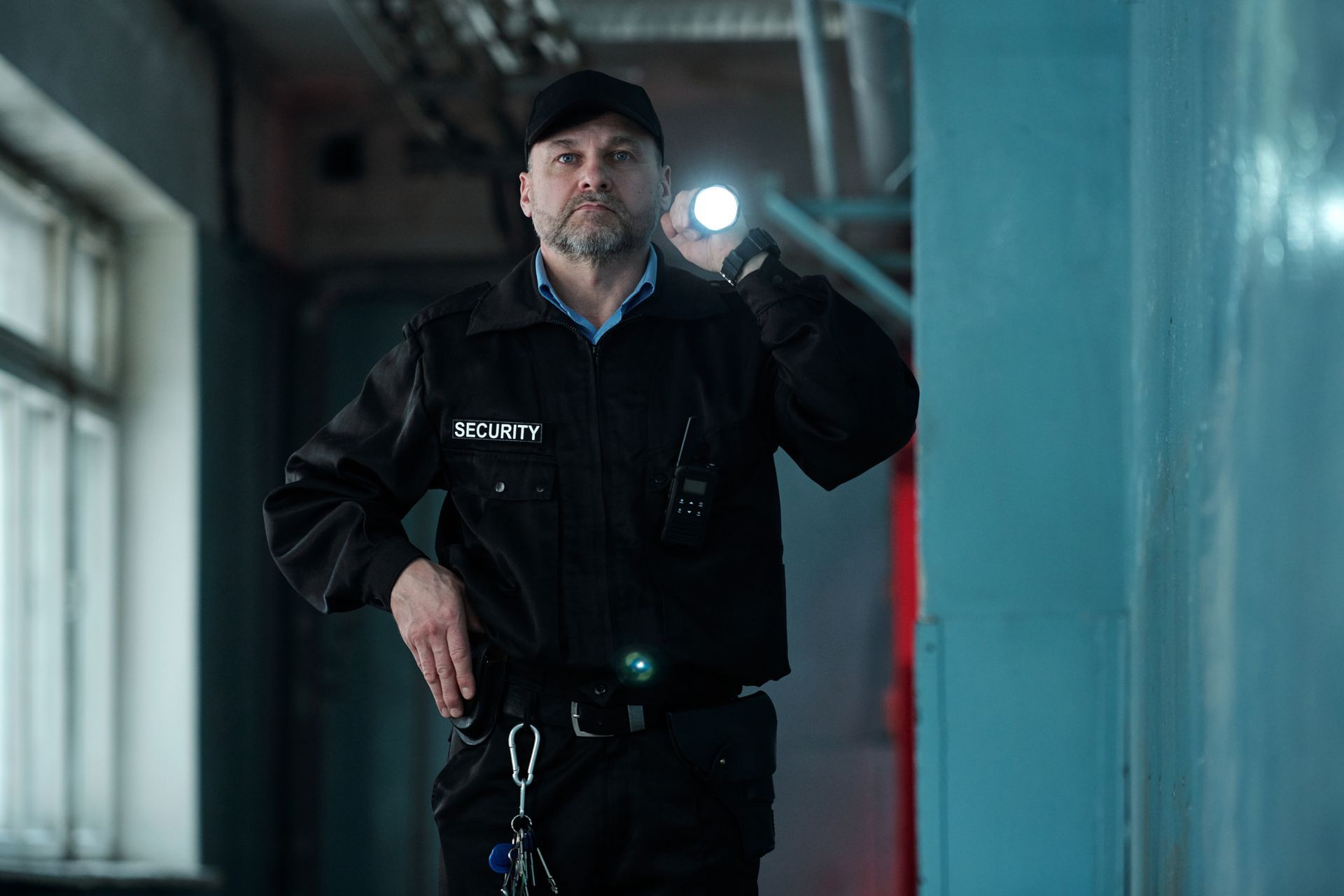 Security guard in black uniform holding a flashlight in a dim industrial hallway