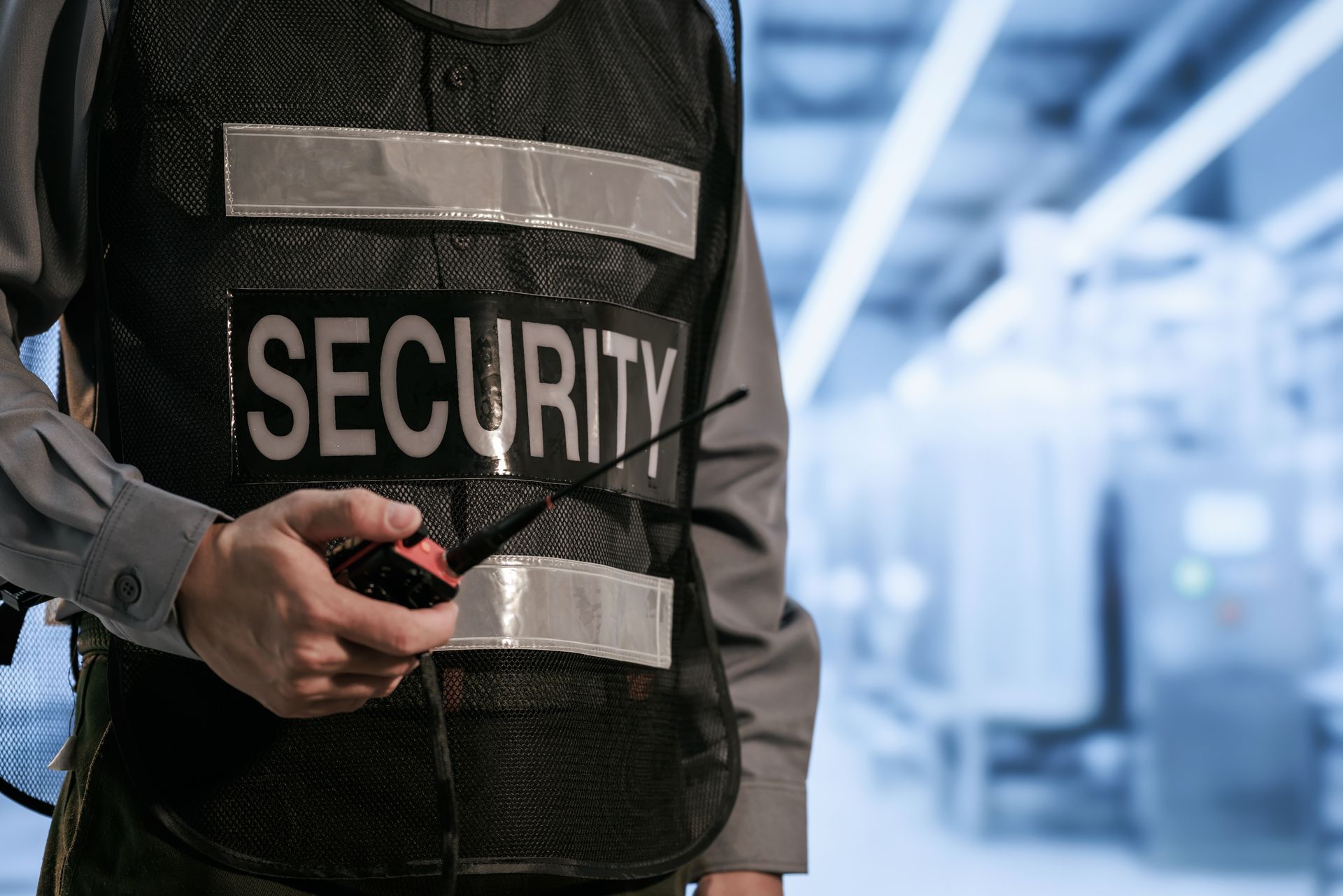 Security guard in dark uniform with reflective vest holding a radio in a bright hallway