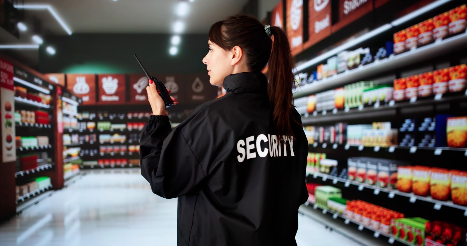 Security guard patrolling a brightly lit grocery aisle and checking shelves with a tablet