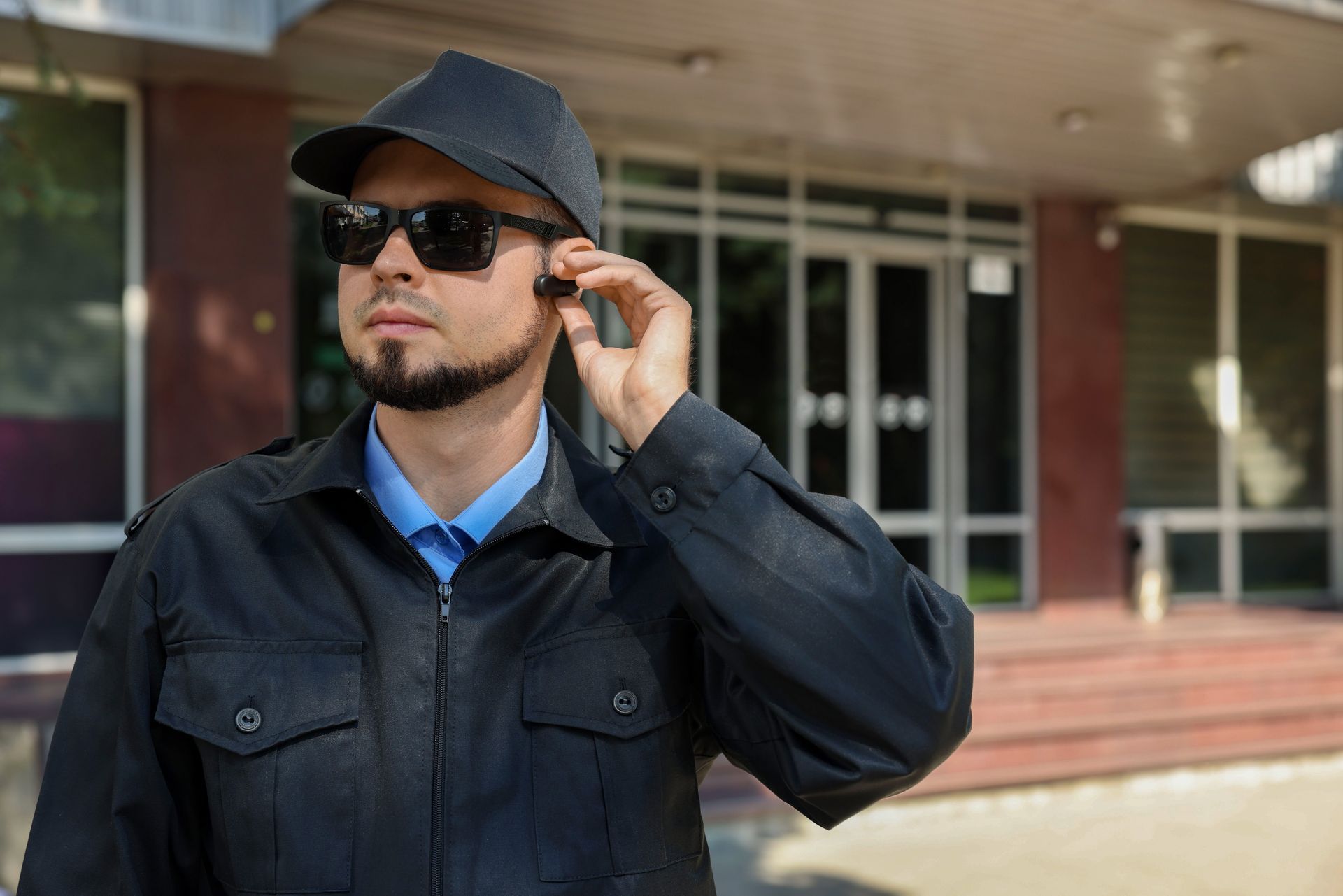 Man in sunglasses and a cap adjusting them outside a building