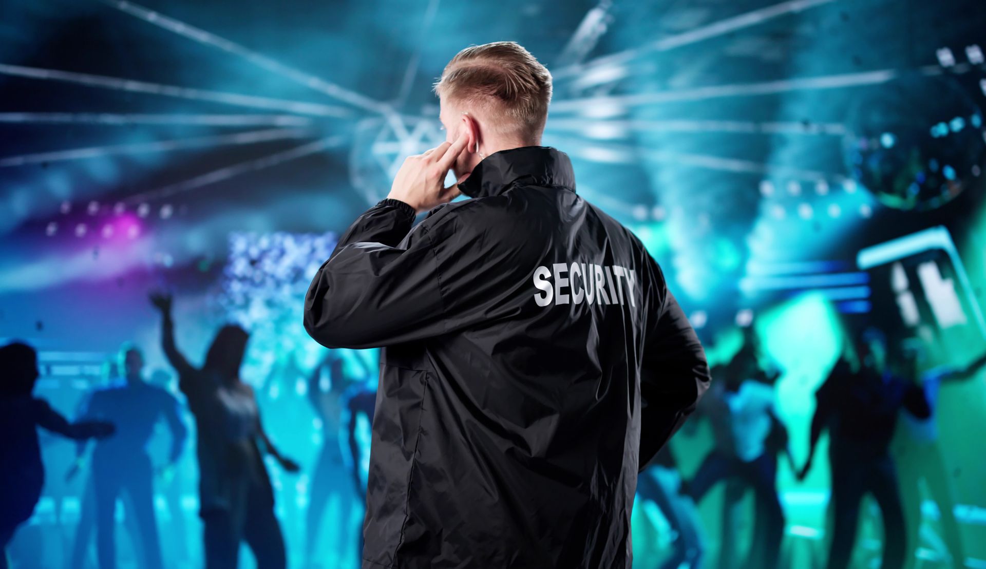 Performer on stage in a black jacket, facing a cheering crowd under blue and purple lights