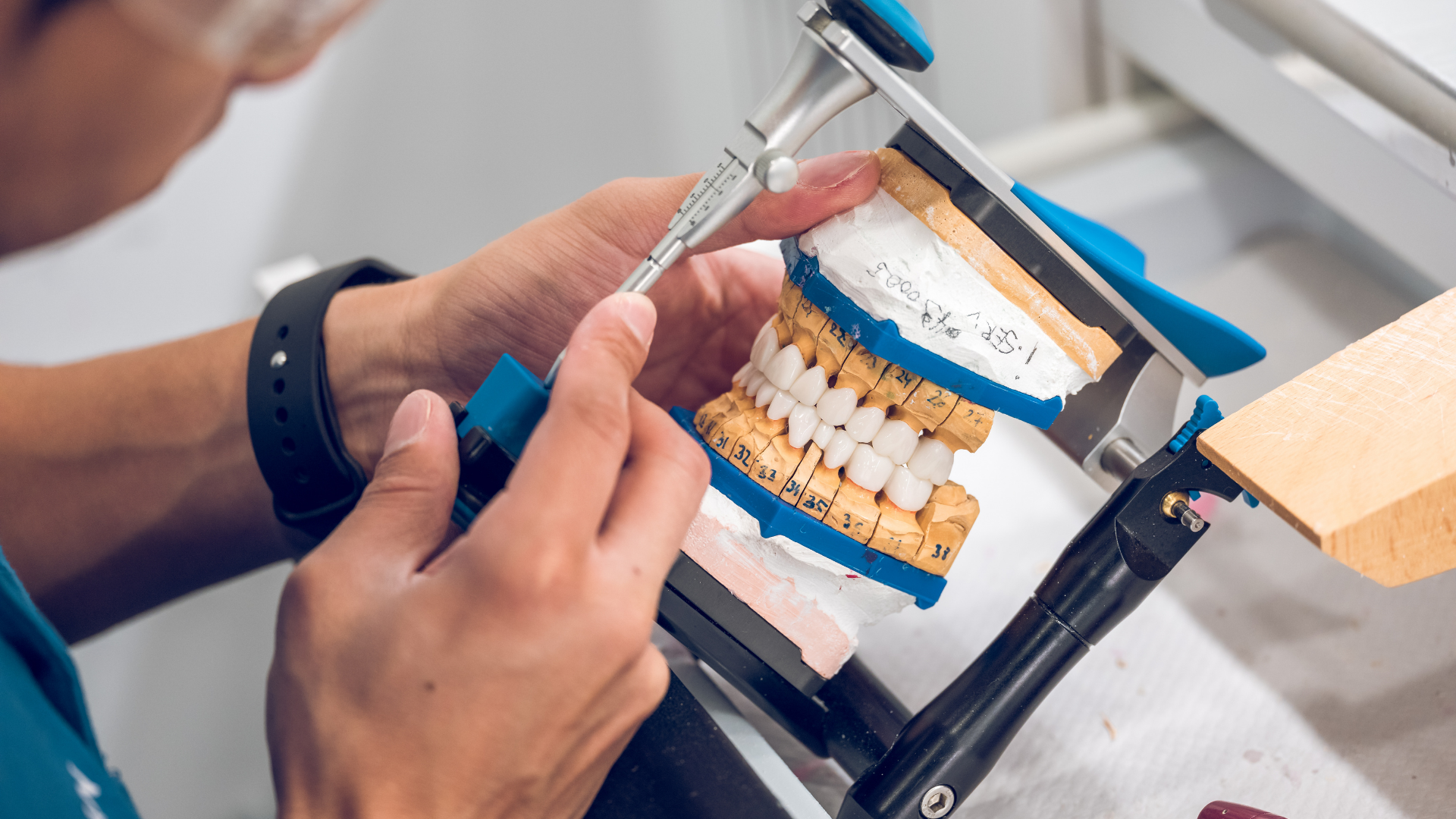 Dentist adjusting a dental prosthetic model with metal tools on a workbench