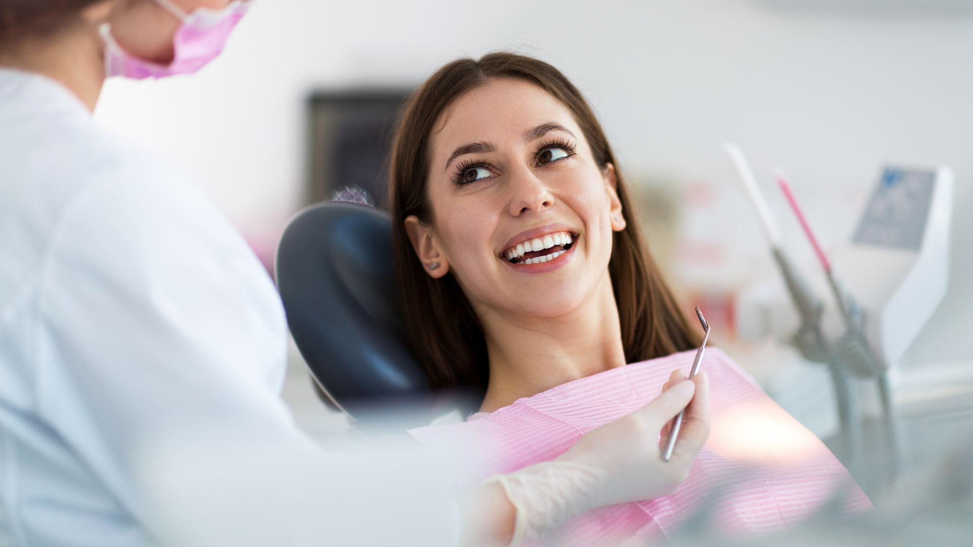 Patient smiling in a dental chair while a dentist in pink gloves works nearby