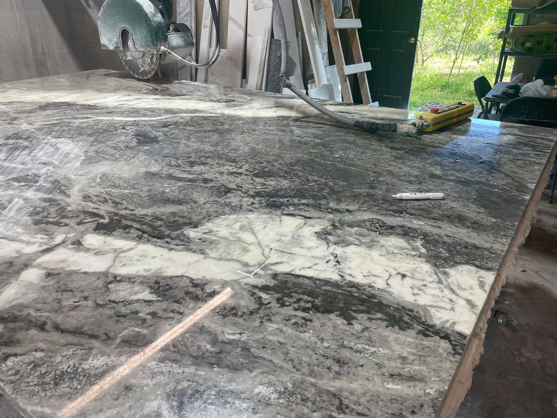 Granite countertop with gray and white veining, tool and wood stick, in a workshop.