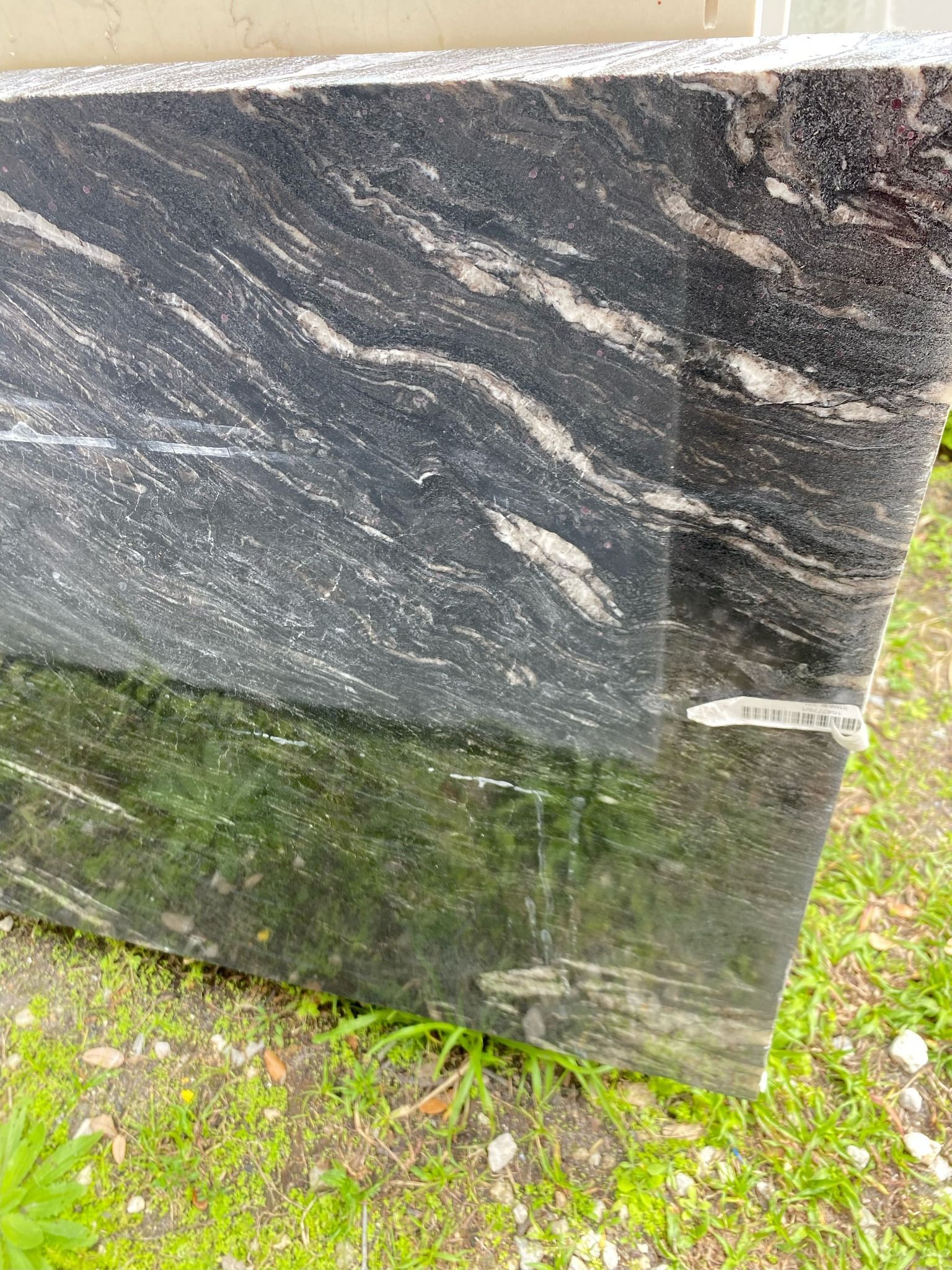 Black granite slab with swirling white and gray patterns, outdoors on grass.