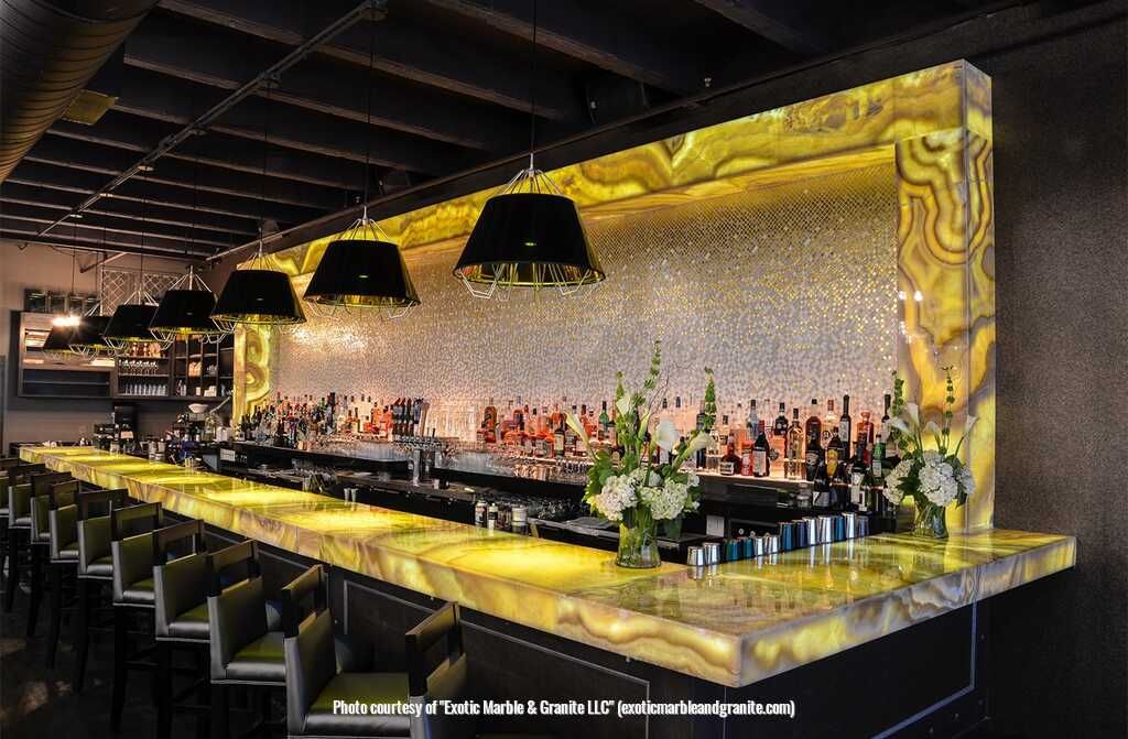 Lit bar with yellow countertop, black lamps, bottles, and bar stools.