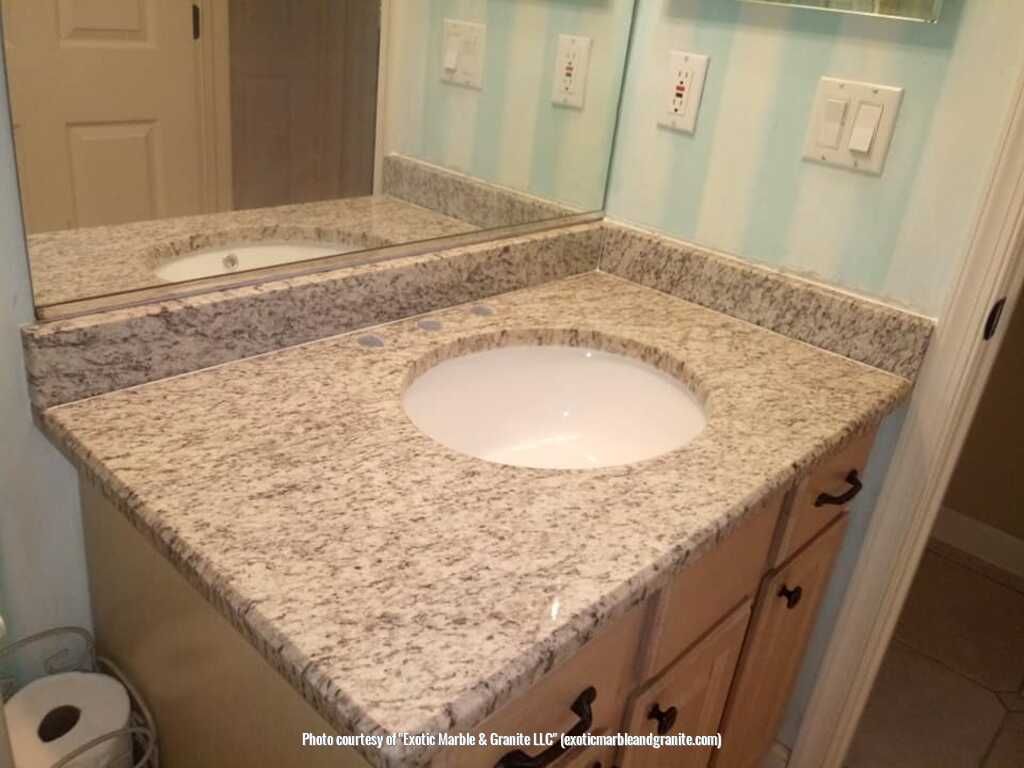 Bathroom vanity with granite countertop and oval sink, light wood cabinets, and large mirror.