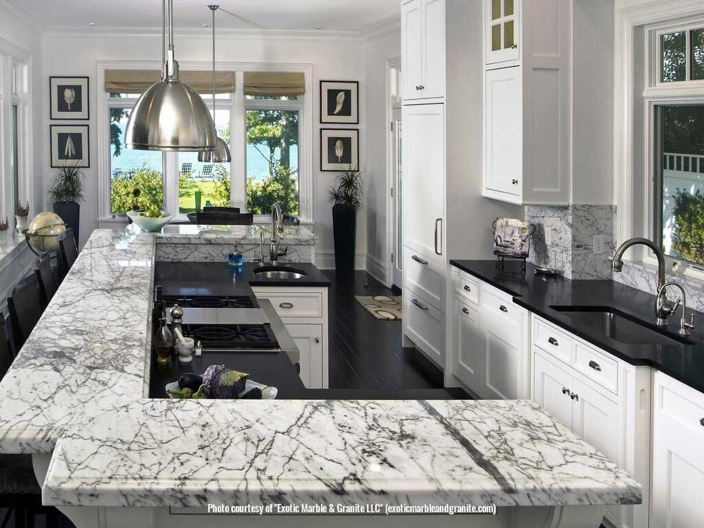 Spacious white kitchen with marble countertops, dark wood floor, stainless steel appliances, and large windows.