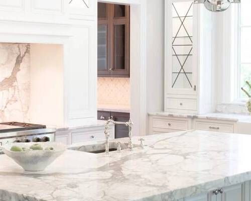 Luxurious white kitchen with marble countertops, cabinets, and a sink.
