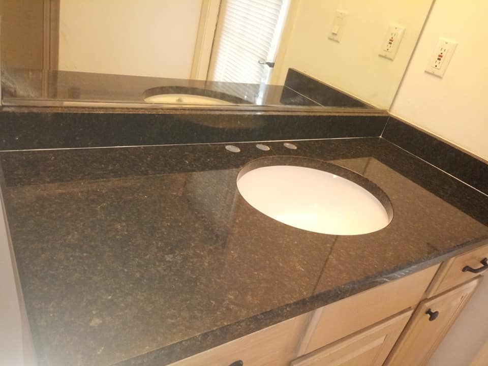 Dark granite countertop with oval sink, beige cabinets, and large mirror.