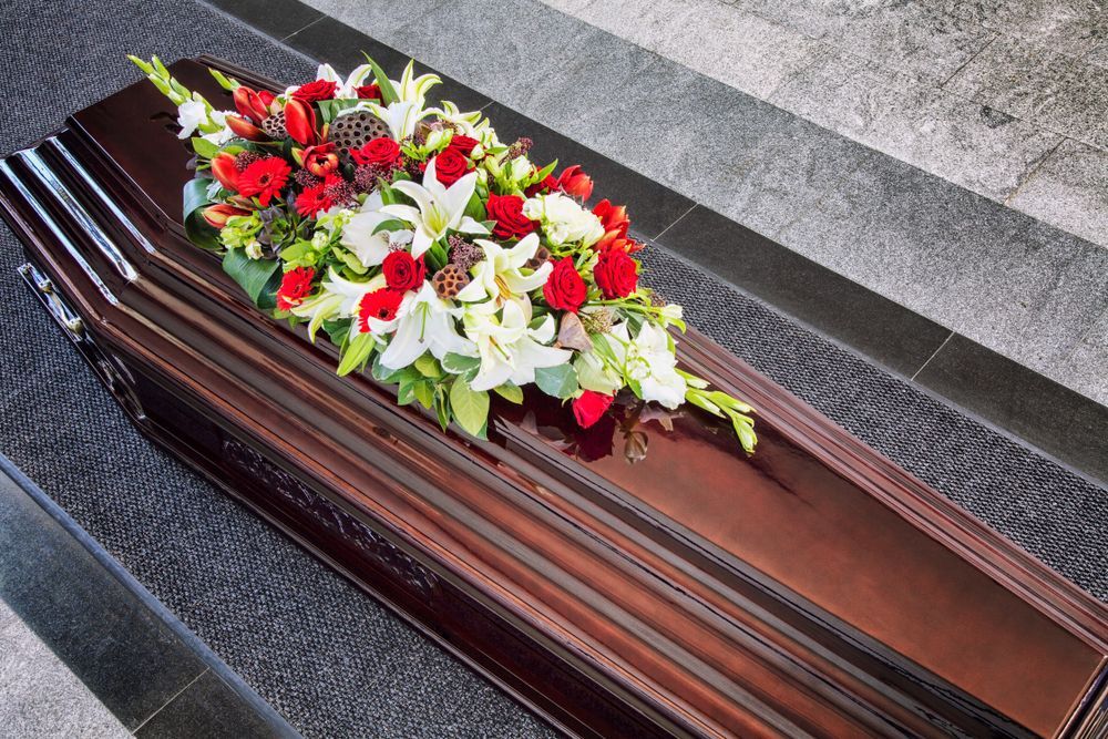 Brown Casket With Flower Arrangement — Finlayson & McKenzie Funeral Directors in Rockhampton City, QLD