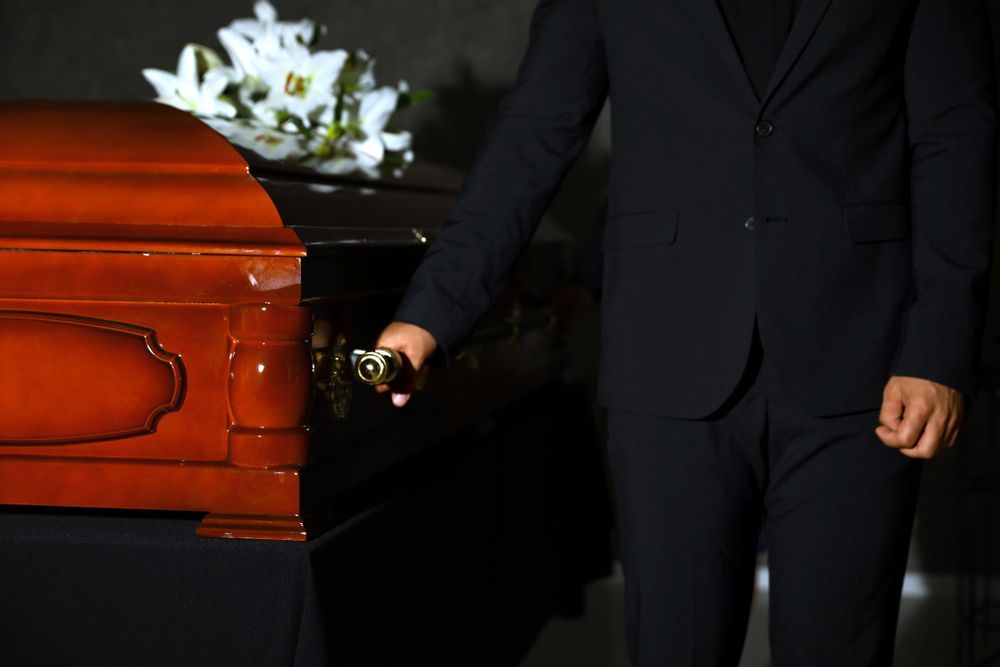 Man in Black Suit Standing Near a Closed Wooden Casket — Finlayson & McKenzie Funeral Directors in Rockhampton City, QLD