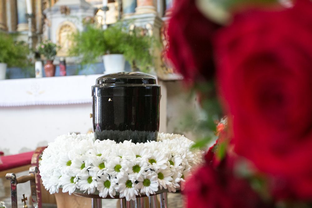 Black Cremation Urn on a White Flower Wreath — Finlayson & McKenzie Funeral Directors in Rockhampton City, QLD