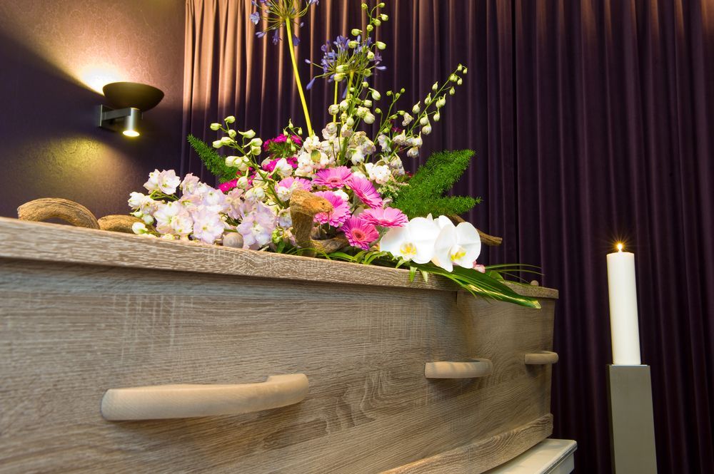 Coffin With Floral Arrangement and Lit Candle — Finlayson & McKenzie Funeral Directors in Rockhampton City, QLD