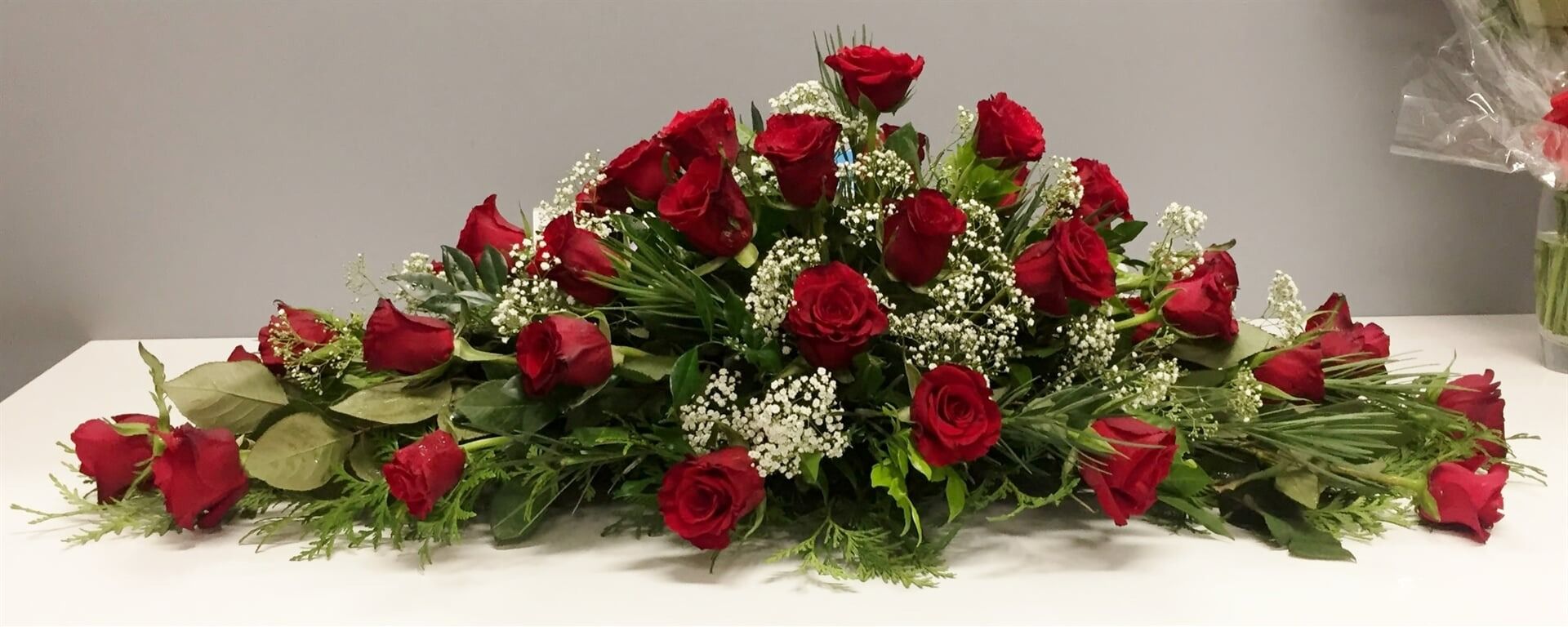 Arrangement of Red Roses and Greenery on a White Surface — Finlayson & McKenzie Funeral Directors in Rockhampton City, QLD